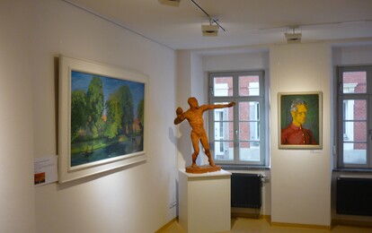 Zu sehen ist ein kleiner Teil einer Ausstellung mit zwei Gemälden und einer Skulptur.