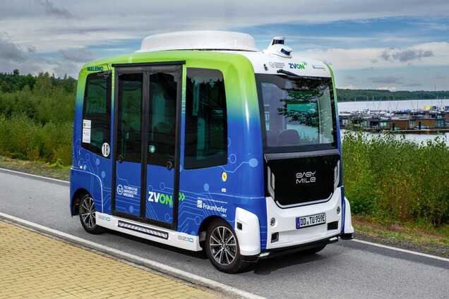 Blau-Weißer moderner Kleinbus fährt nahe eines Sees entlang