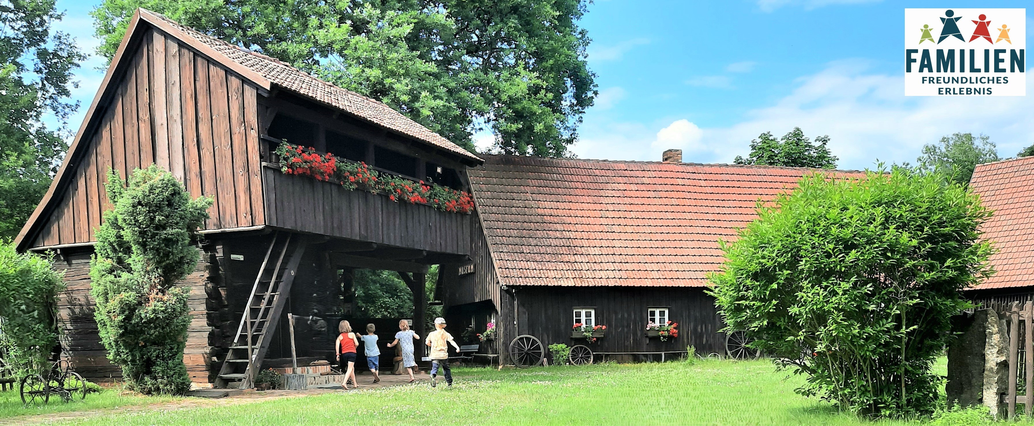 Kinder vor altem Gehöft aus Holz mit Garten